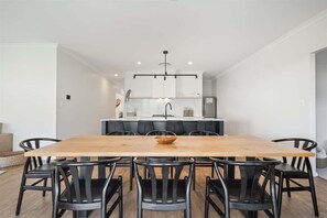 Ein Essbereich mit Holztisch und schwarzen Stühlen, im Hintergrund eine Küche und eine moderne Pendelleuchte.
