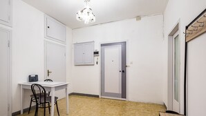 Una stanza con una scrivania bianca, due sedie, un lampadario, una porta e una panca.