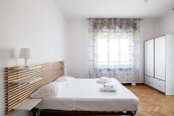 A hotel room with a bed, bedside tables, a wardrobe, and a window with a curtain. - Quiet and Cozy Urban Apartment by Wonderful Italy (Bologna)