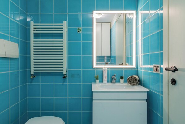 A bathroom with blue tiles, a white sink, a mirror, and a towel rack. - Loft Augusta a Piazza Castello by Wonderful Italy (Turin)