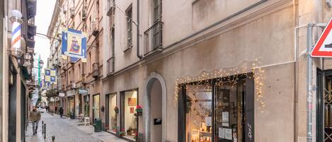 A cobblestone street with storefronts, including a shop with string lights and a visible sign.
