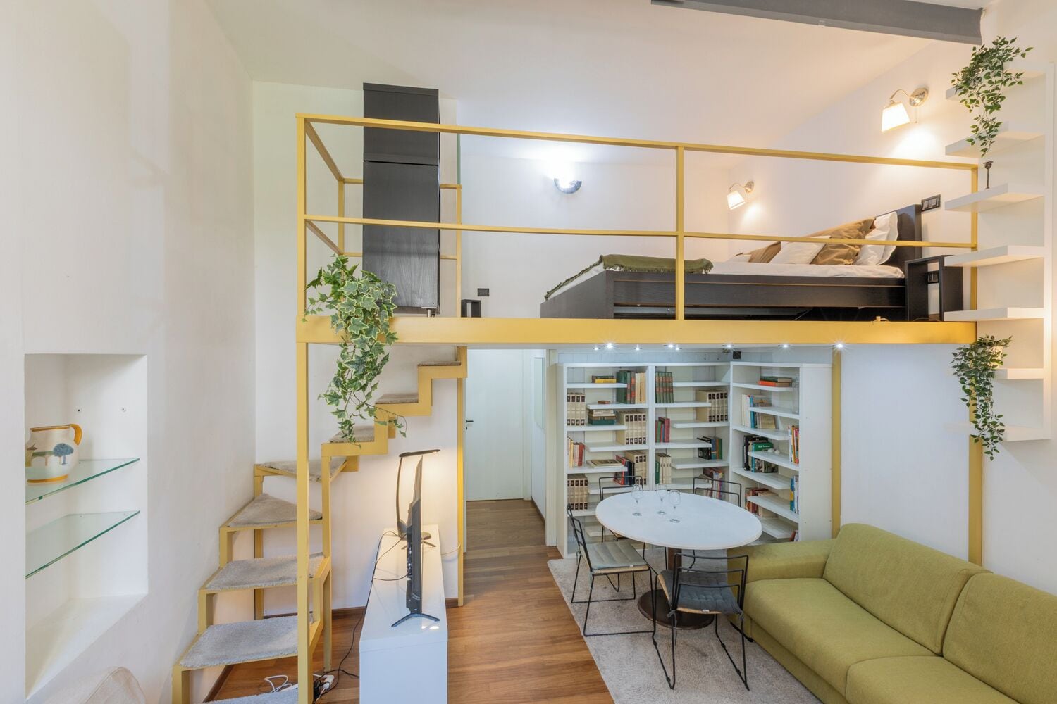 A compact living space with a loft bed, a dining area with a round table, and a green sofa.