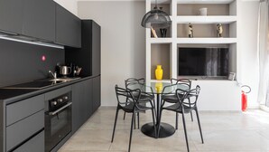 A modern kitchen with black cabinetry, a dining table with chairs, a pendant light, and a flat-screen TV on a shelf. - Design Suite in Bologna by Wonderful Italy (Bologna)
