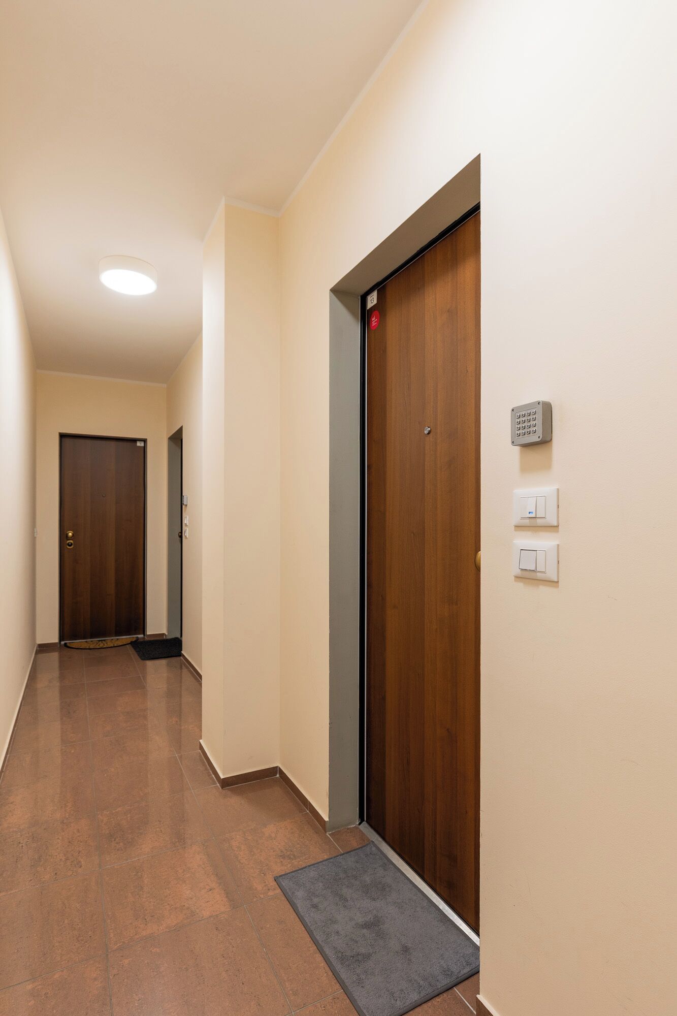 A hallway with a wooden door, a keypad lock, and a doormat.