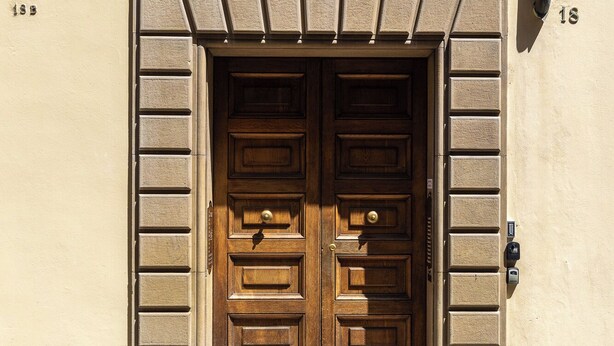 A double wooden door with a stone frame, set in a beige building with a stone base. - Design Suite in Bologna by Wonderful Italy (Bologna)
