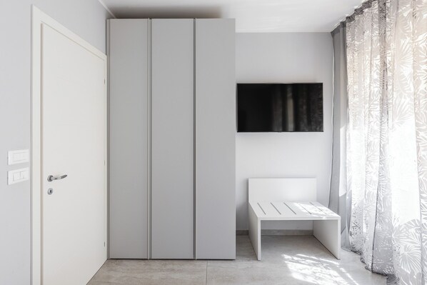 A modern bedroom with a wardrobe, a flat-screen TV mounted on the wall, and a bench. - Design Suite in Bologna by Wonderful Italy (Bologna)
