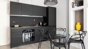 A modern kitchen with dark cabinetry, a gas stove, a built-in oven, and a glass dining table with black chairs. - Design Suite in Bologna by Wonderful Italy (Bologna)