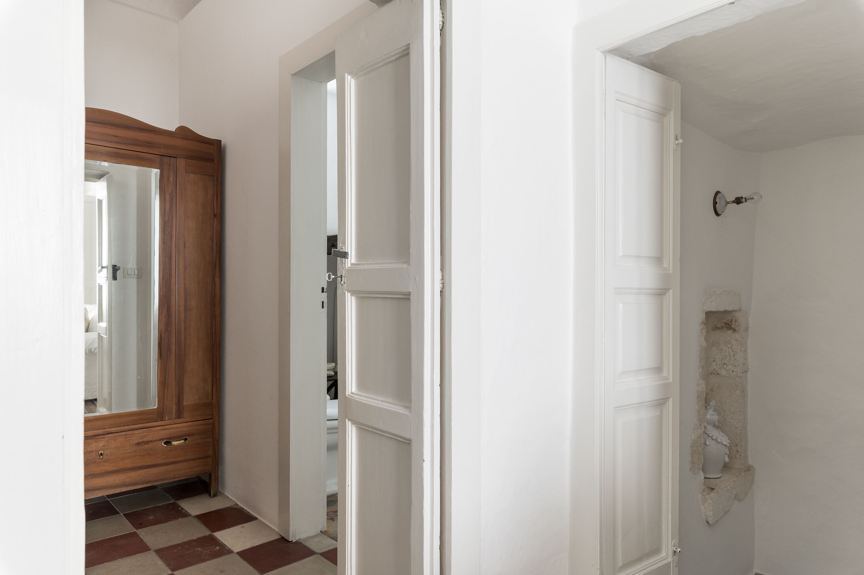 A hallway with a checkered floor, a wooden wardrobe, and a white door with a stone wall feature.