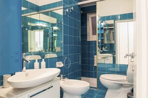 A modern bathroom with blue tiles, a large mirror, a sink, a bidet, and a toilet. - Eden Vista Mare con Piscina by Wonderful Italy  (Genoa)
