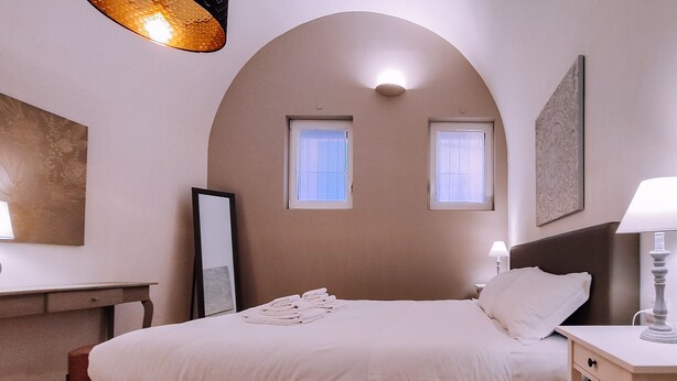 Ein Schlafzimmer mit einem Bett, Nachttischen, einem Schreibtisch und zwei Fenstern.