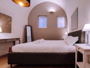 A bedroom with a bed, bedside tables, a desk, and two windows. - Elegante Appartamento Alle Due Torri By Wonderful Italy (Bologna)