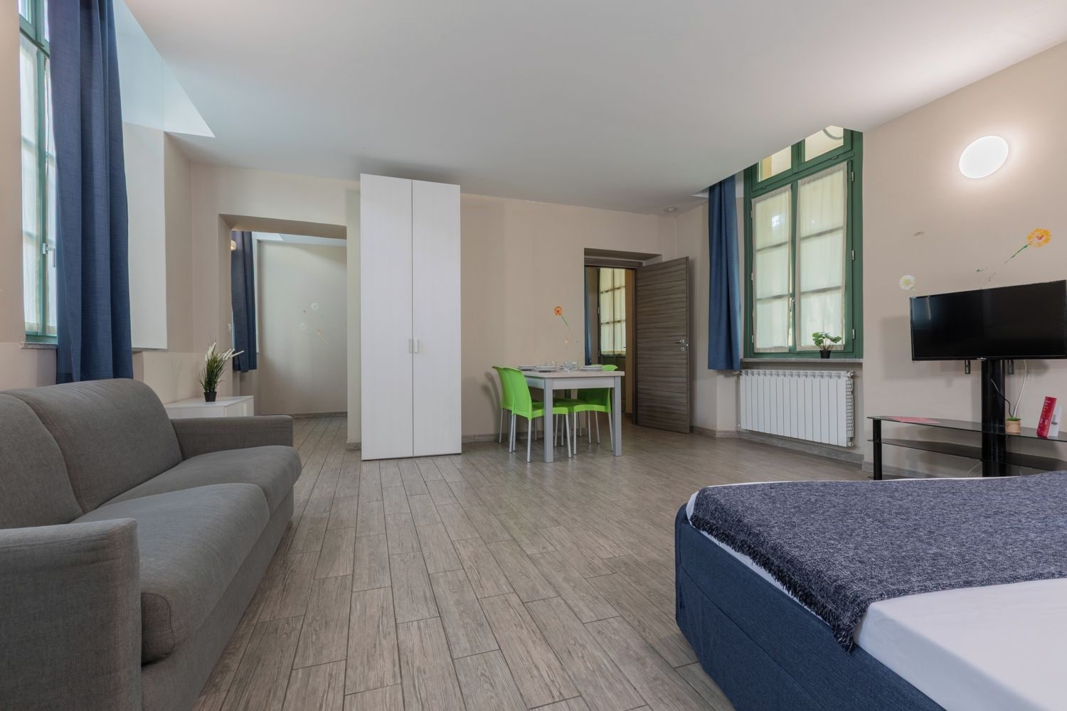 A hotel room with a bed, a sofa, a desk with a chair, and a television.