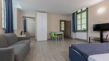 A hotel room with a bed, a sofa, a desk with a chair, and a television.