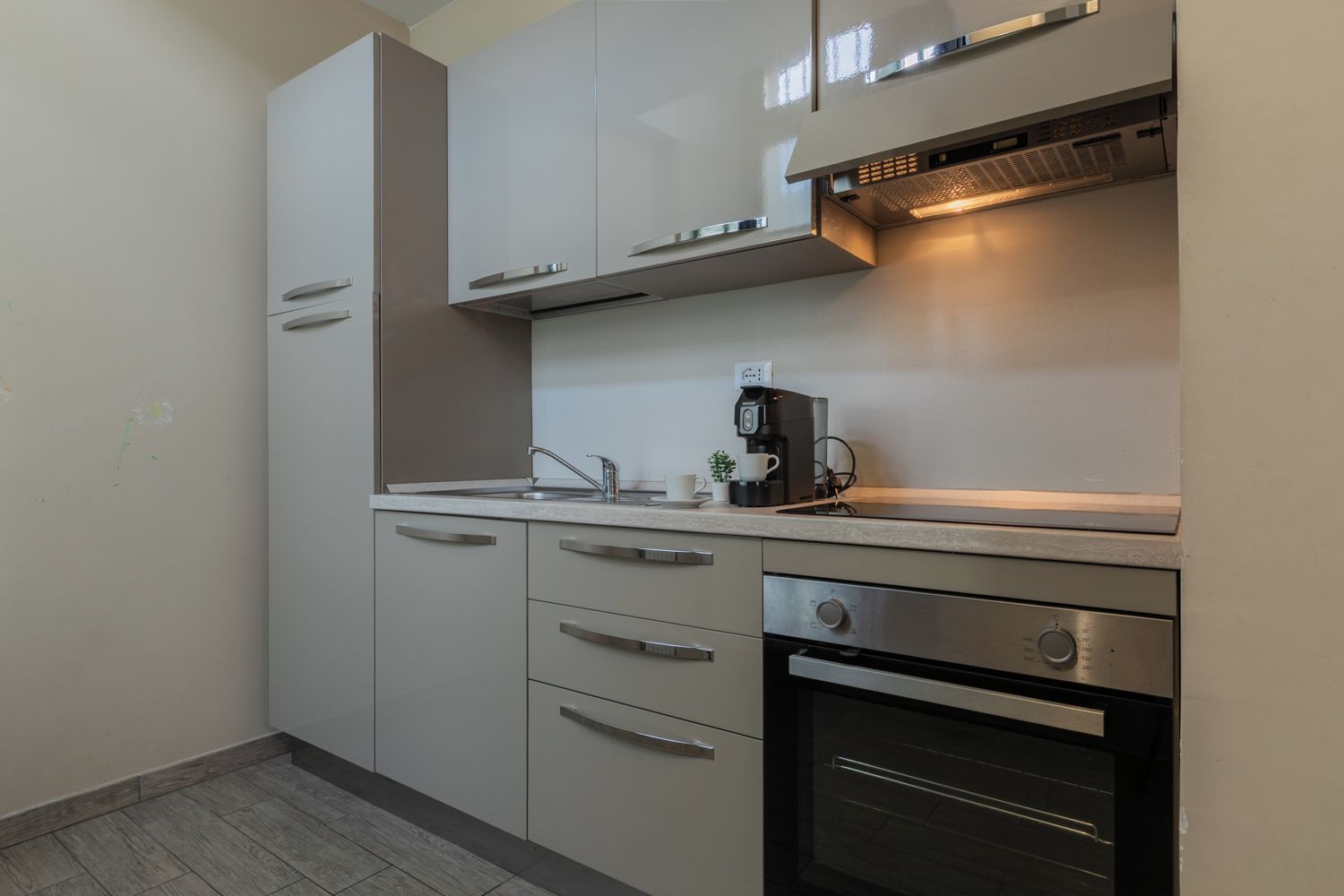 Una cucina compatta con forno integrato, macchina del caffè e lavello.
