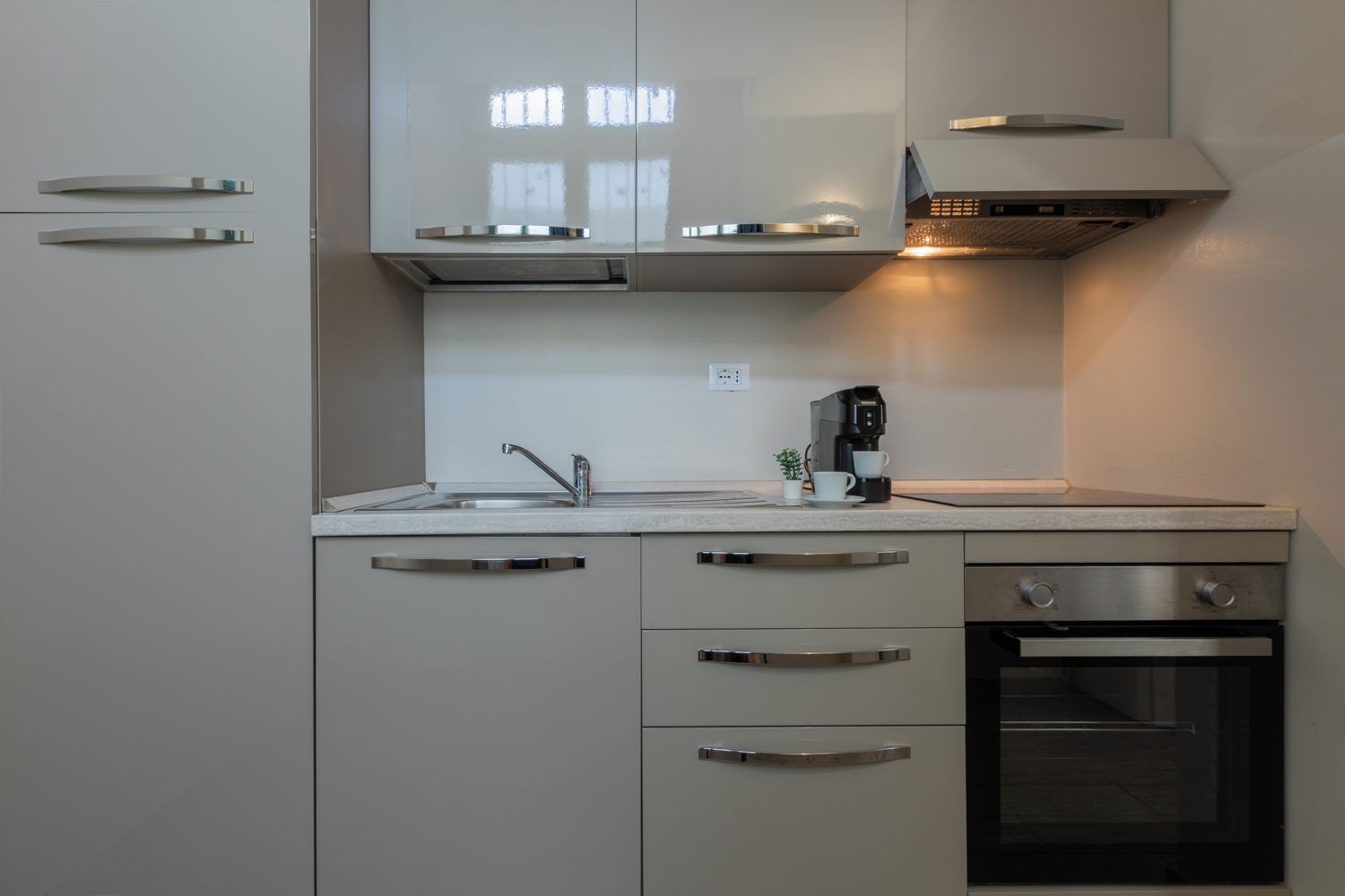 Una cocina moderna con horno empotrado, cafetera y ventana sobre el fregadero.
