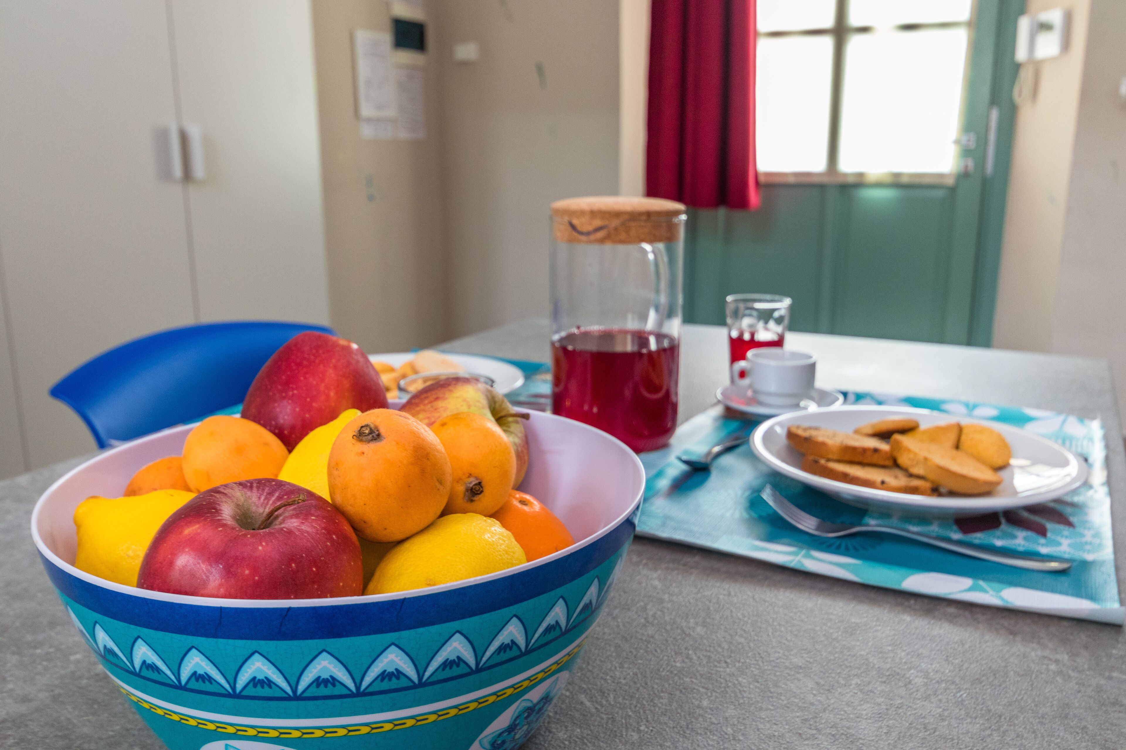 Eine Schüssel Obst, ein Glas roter Saft und ein Tablett Kekse auf einem Tisch.