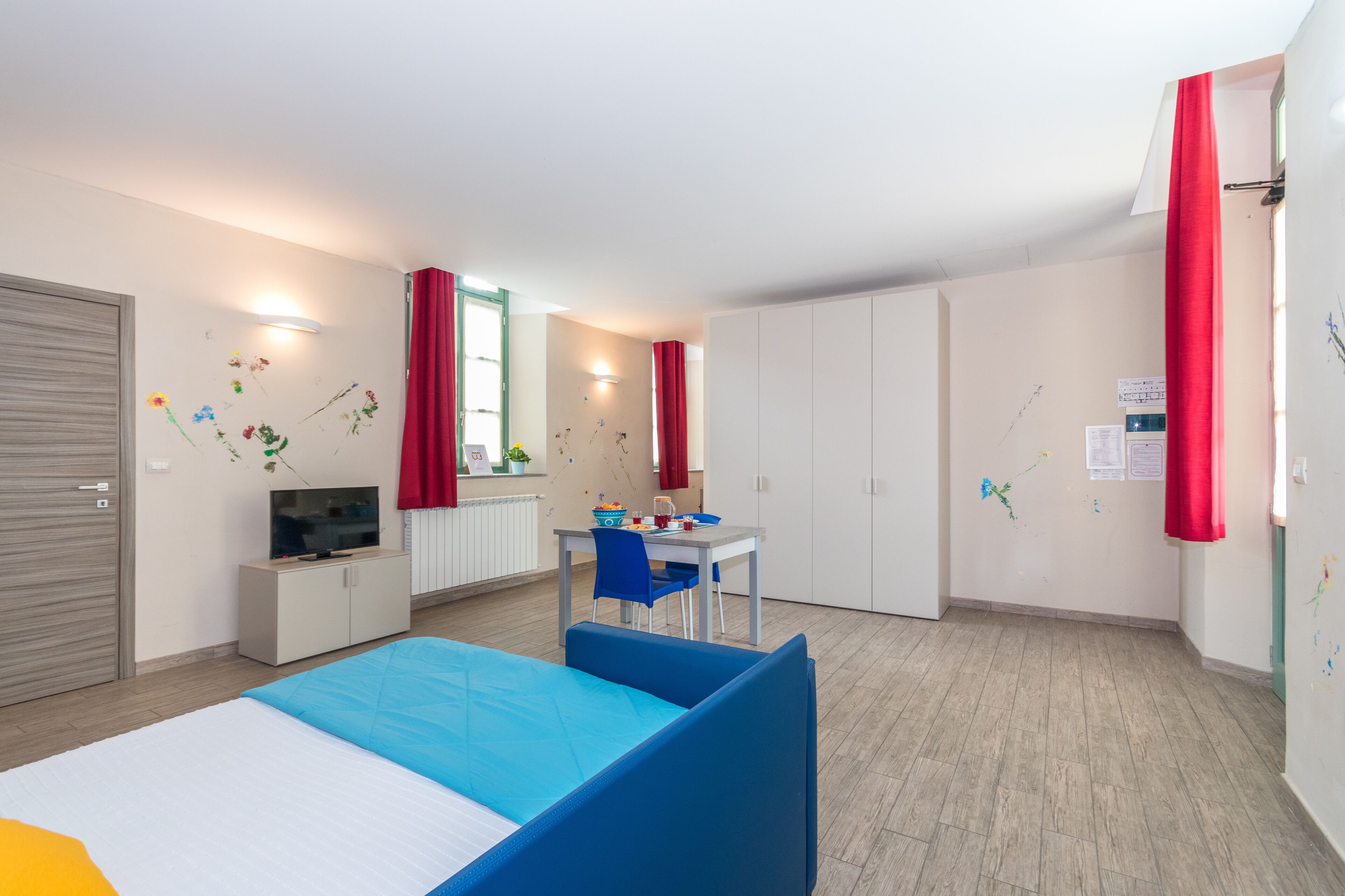 A modern hotel room with a bed, a desk, a TV, and a wardrobe.