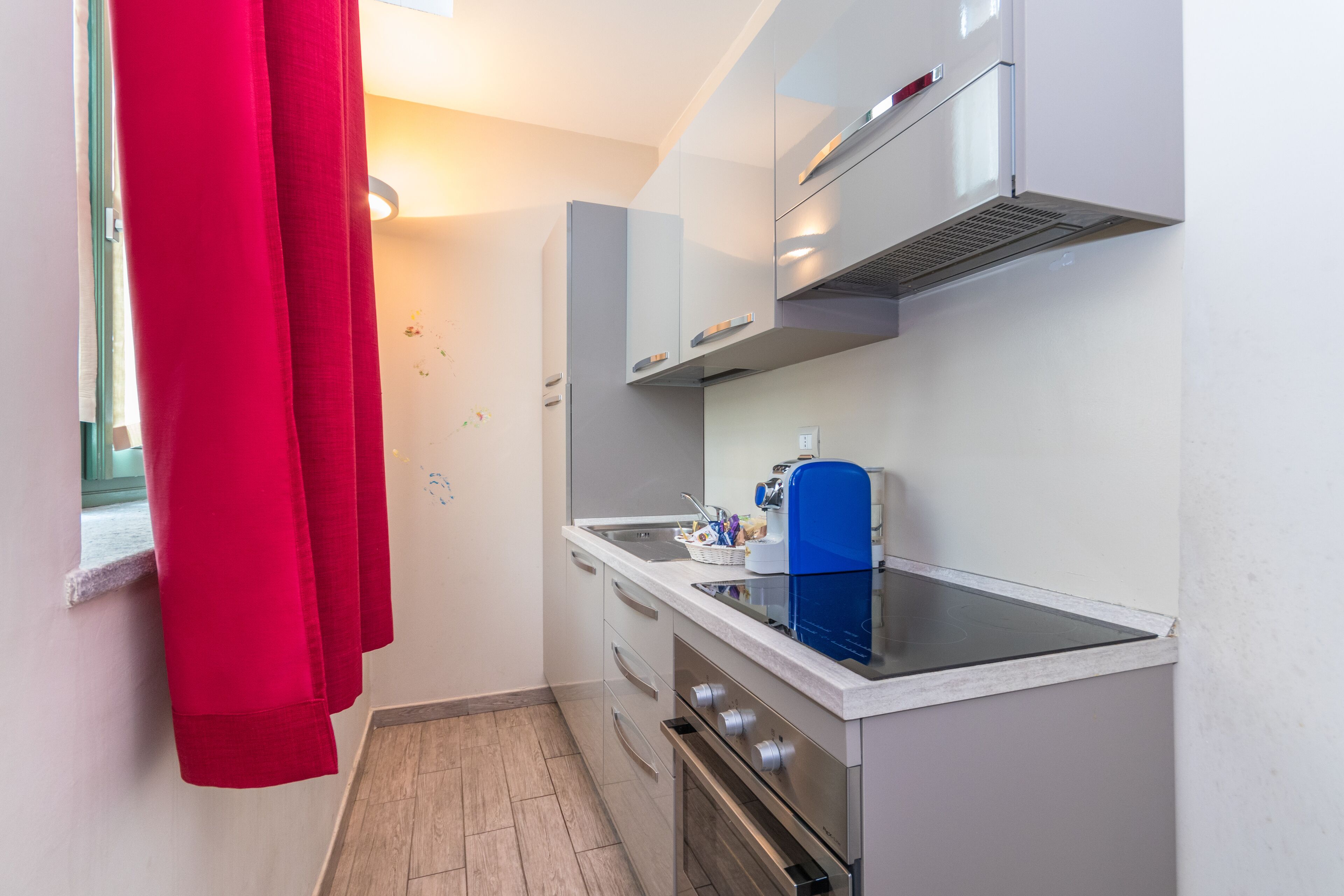 A compact kitchen with white cabinets, a stainless steel oven, and a blue coffee machine.