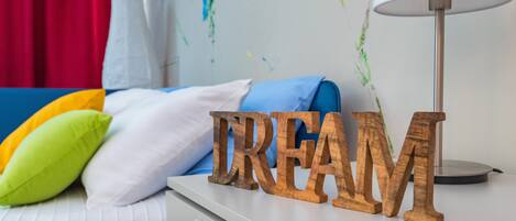 A bed with a white headboard, a blue pillow, and a green pillow. There is a wooden sign with the word "DREAM" on a white nightstand.