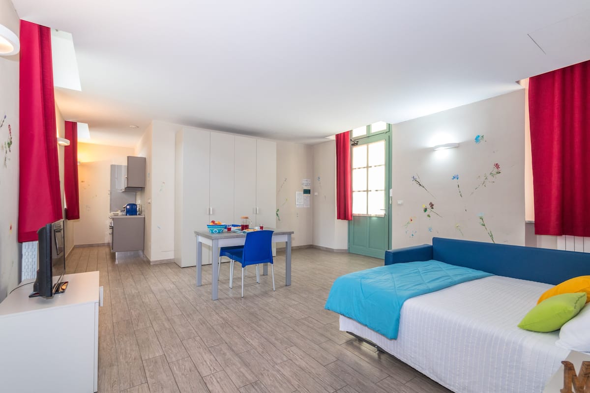 A modern bedroom with a bed, a desk, and a kitchenette.