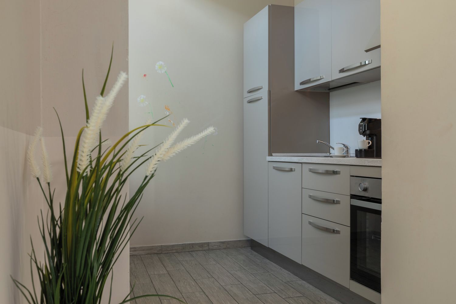 A kitchen with white cabinets, a coffee maker, and a potted plant with white flowers.