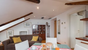 Una sala de estar acogedora con una mesa de comedor dispuesta para el desayuno, un sofá con cojines y una cocina visible a través de un umbral abierto.