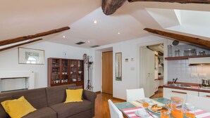 Una sala de estar acogedora con un sofá marrón, una mesa de comedor lista para el desayuno y una cocina al fondo.