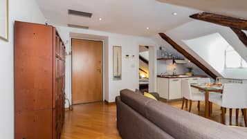 Une cuisine moderne avec des meubles en bois, un coin repas avec une table et des chaises, et une chambre en mezzanine avec un plafond en pente.