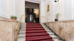 Una imponente escalera con paredes de mármol y peldaños cubiertos de alfombra roja.