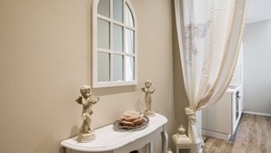 A white console table with decorative statues, a rose-shaped centerpiece, and a window above. - Maison Del Reno By Wonderful Italy (Bologna)