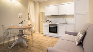 A modern kitchen with white cabinets, a built-in oven, and a dining area with a round table and clear chairs. - Maison Del Reno By Wonderful Italy (Bologna)