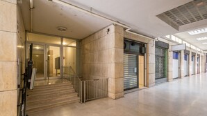 A spacious lobby with a staircase leading to an elevator, a glass door entrance, and a closed shop with a metal shutter. - Maison Del Reno By Wonderful Italy (Bologna)