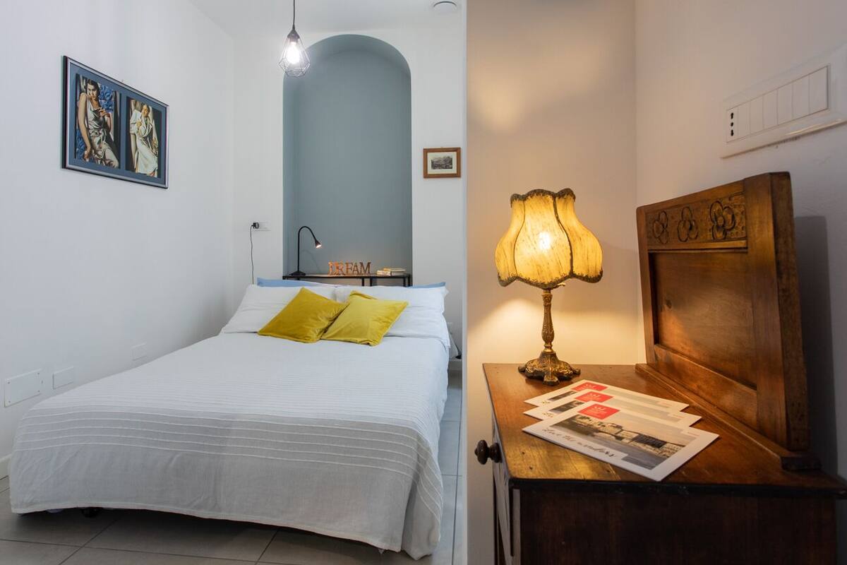 A bedroom with a bed, a nightstand, a lamp, and a wall-mounted shelf.