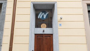 A building facade with a wooden double door, a window with a logo and the number 16, and a blue sign with the number 16. - Rosso E Blu Di San Salvario By Wonderful Italy (Turin)