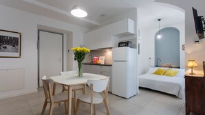 A modern kitchen with white cabinets, a dining area with a white table and chairs, and a bedroom with a bed and a nightstand. - Rosso E Blu Di San Salvario By Wonderful Italy (Turin)
