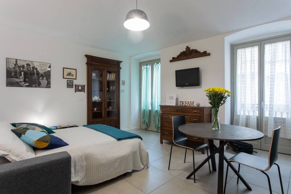 A room with a bed, a desk, a chair, a dining table, and a TV on the wall.
