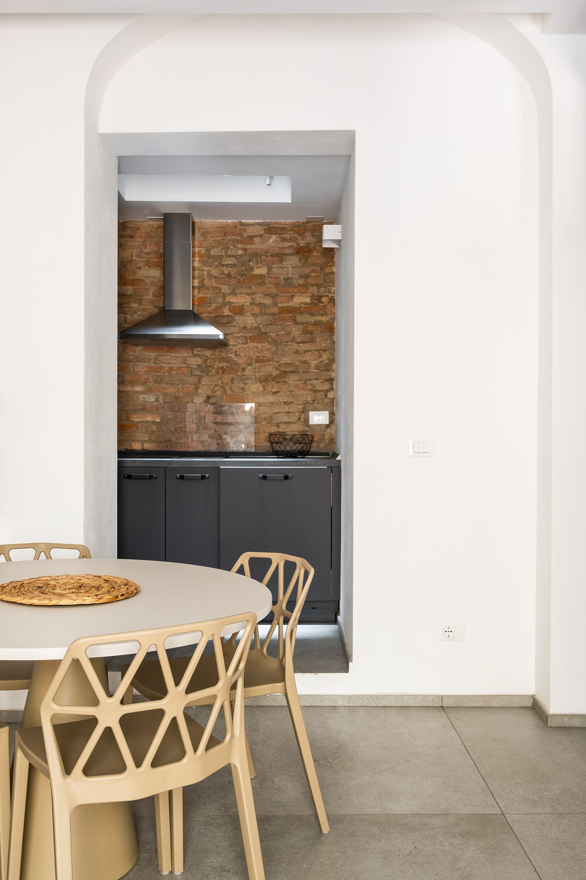 A modern kitchen with a brick wall, dark cabinets, and a round table with chairs.