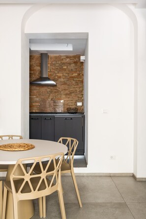 A modern kitchen with a brick wall, dark cabinets, and a round table with chairs. - San Michele Apartments By Wonderful Italy (Bologna)