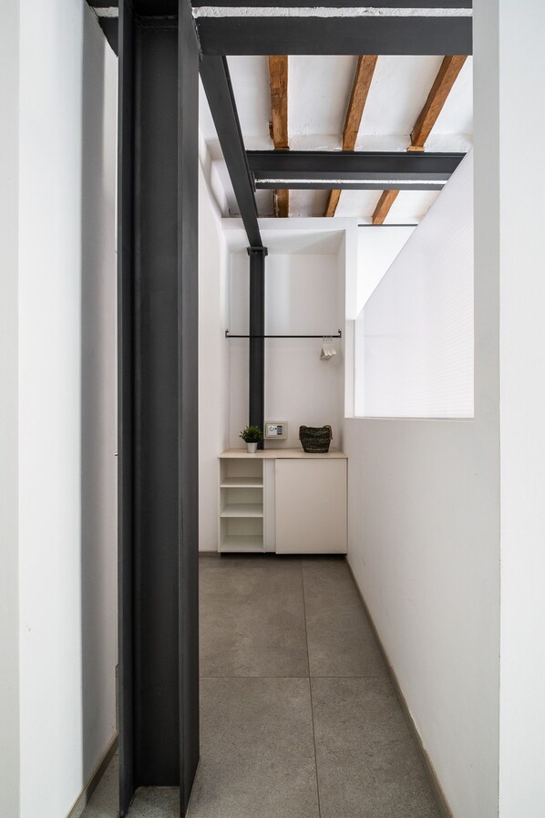 A narrow hallway with a dark door frame, a white cabinet with a small plant, and a window with blinds.