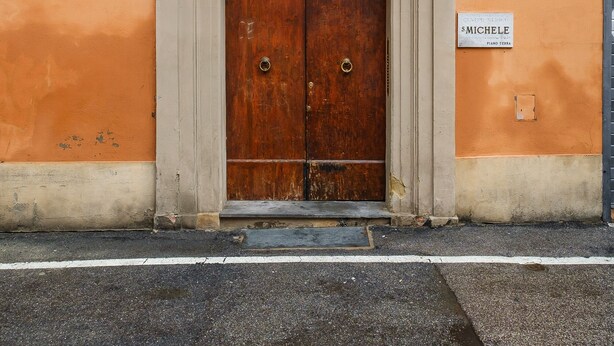 A building facade with a wooden door, a balcony with metal railings, and a sign indicating 'Piazza San Michele'.
