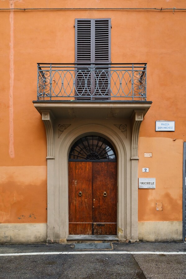 Fachada de edificio con puerta de madera, un balcón con barandilla metálica y un cartel que indica 'Piazza San Michele'.