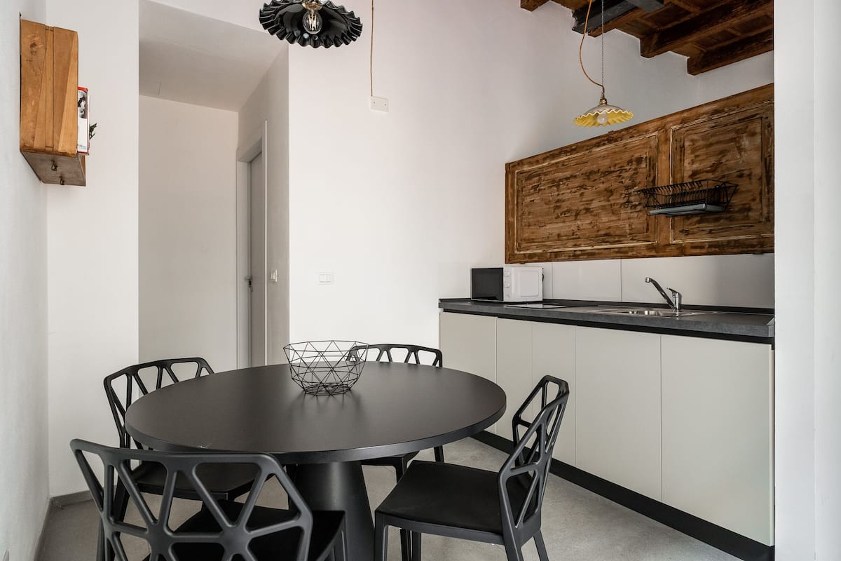 A modern kitchen with a round dining table, black chairs, and a wooden cabinet above the counter.