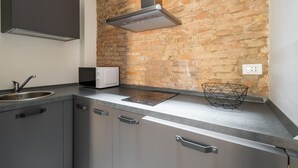 A kitchen with a brick wall, stainless steel cabinets, a microwave, and a modern range hood.