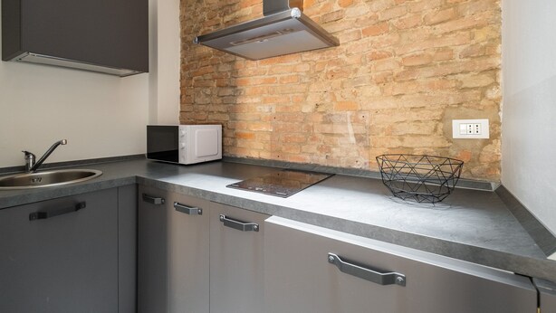 Una cocina con pared de ladrillo, armarios de acero inoxidable, microondas y una campana extractora moderna.