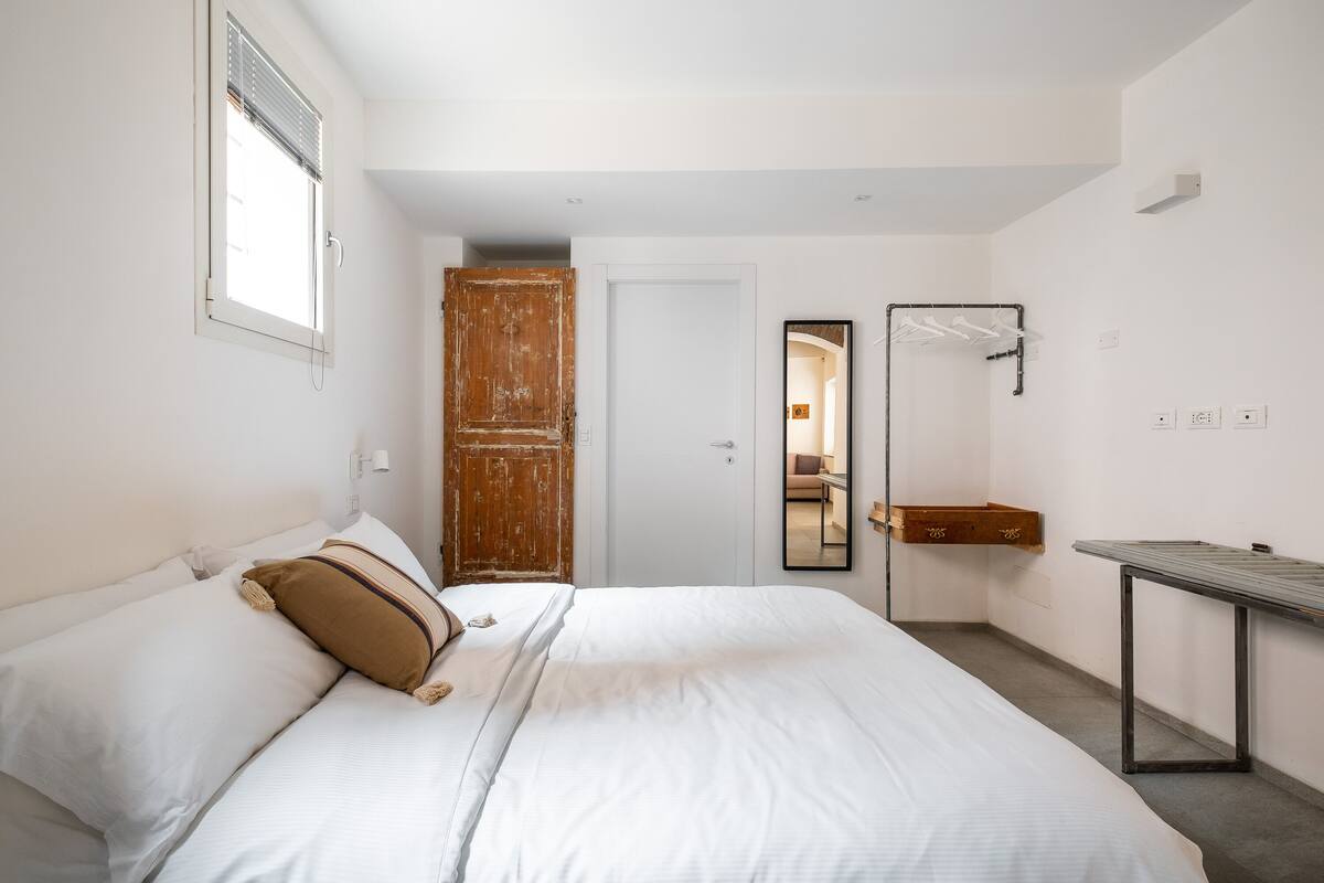 A bedroom with a large bed, a wooden wardrobe, a mirror, and a small table.