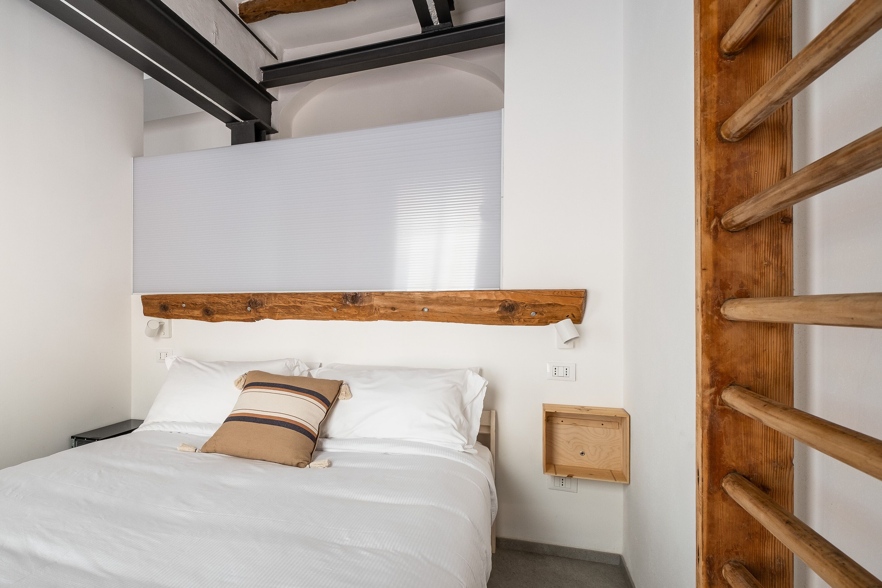 Un dormitorio con cama, cabecera de madera, mesitas de noche y una lámpara fijada a la pared.