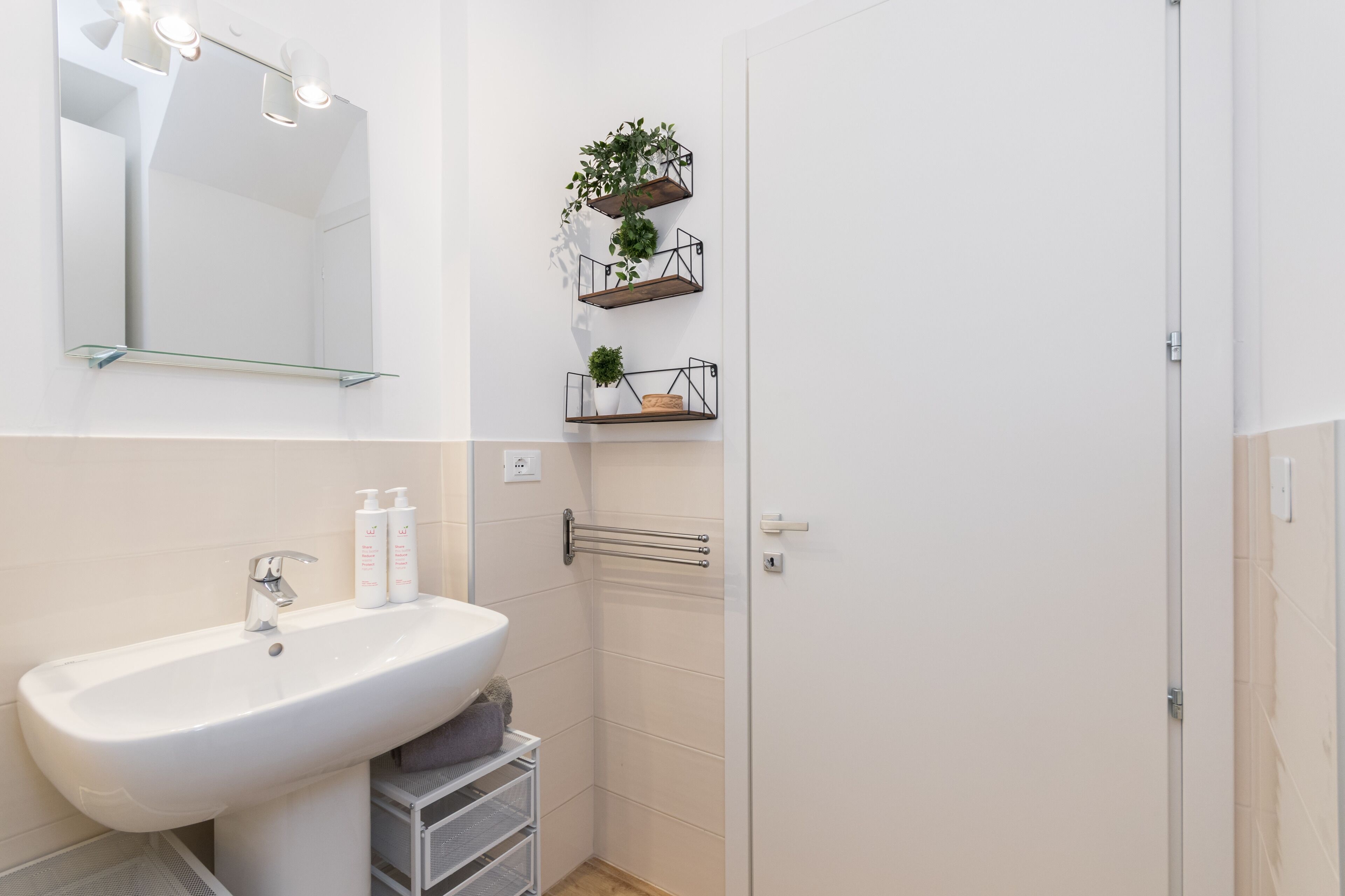 Une salle de bain avec un lavabo blanc, un miroir et trois étagères ornées de plantes.