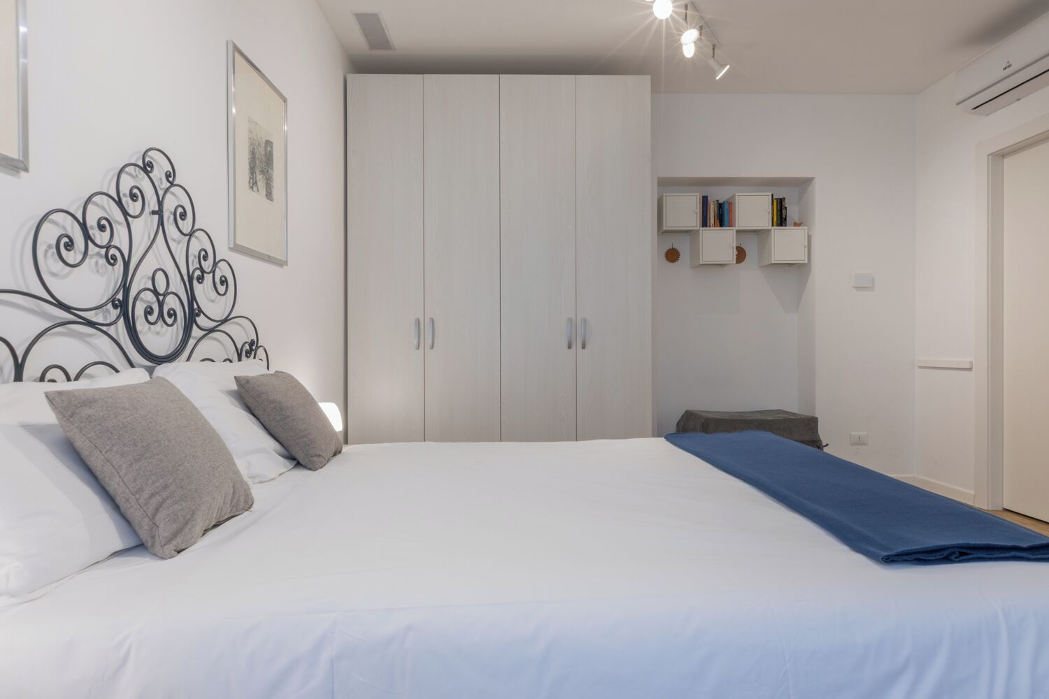 Een slaapkamer met een bed, een garderobe en een klein plankje met boeken.
