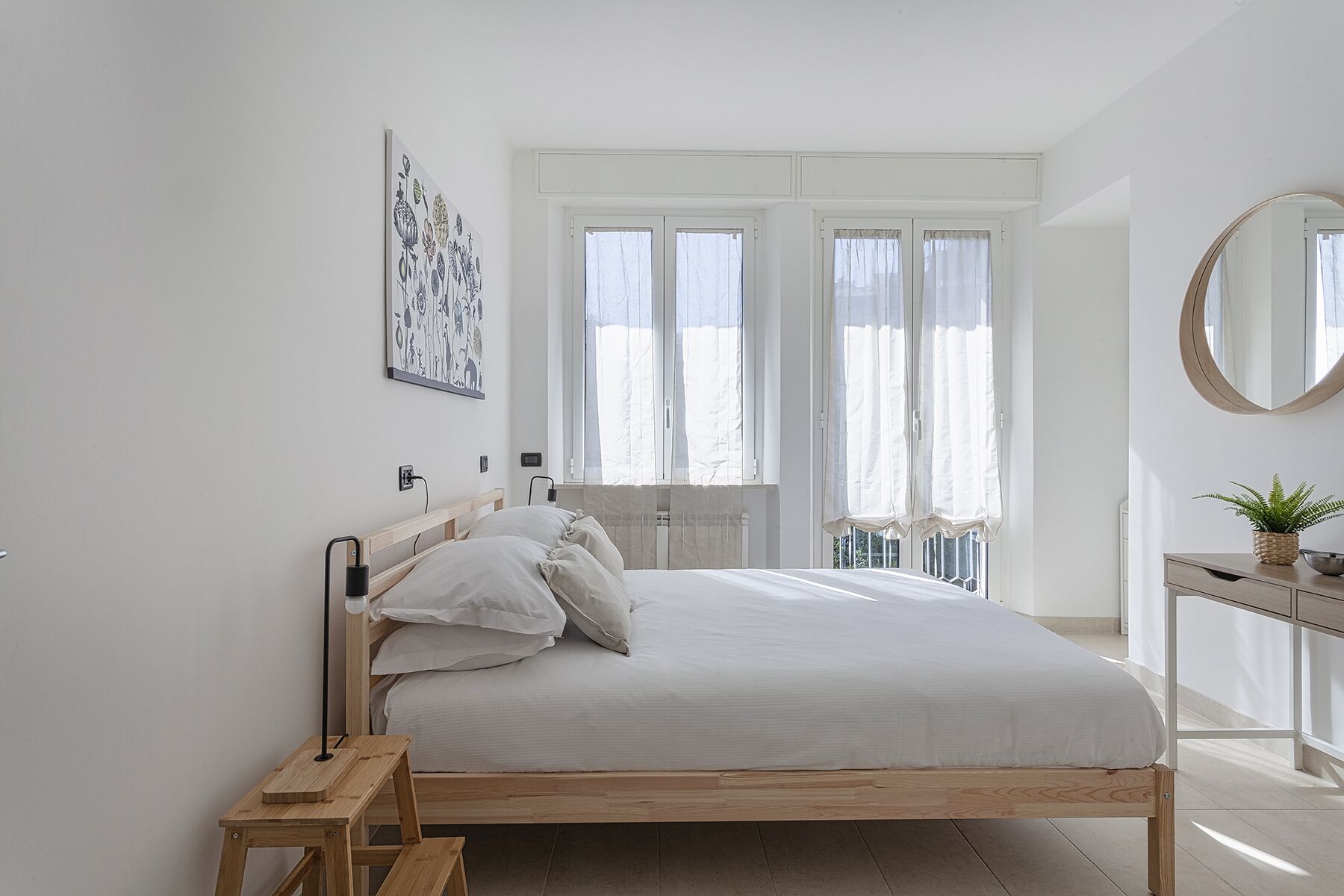 Une chambre à coucher au style minimaliste, avec un lit en bois, une table de chevet, un miroir et une fenêtre avec des rideaux.