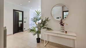 A hallway with a potted plant, a round mirror, and a white console table.